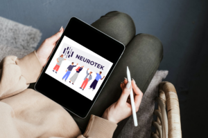 A person holding a tablet displaying the Neurotek logo and an illustration of people on the screen, holding a stylus pen in a cozy indoor setting.